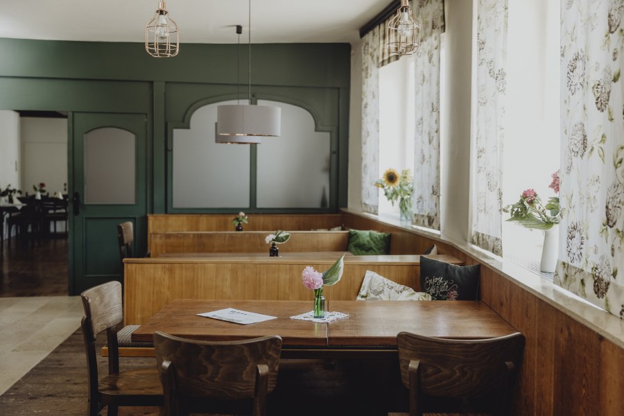 Innenansicht eines traditionellen Wirtshauses mit Holzm&ouml;beln und Blumen auf den Tischen.