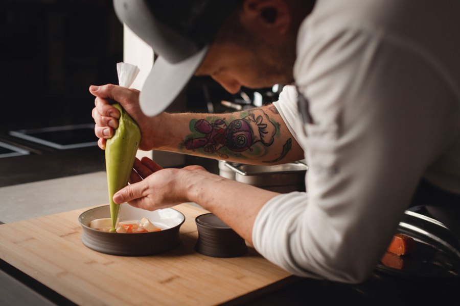 Ein Koch dekoriert ein Gericht mit einer grünen Sauce aus einem Spritzbeutel.
