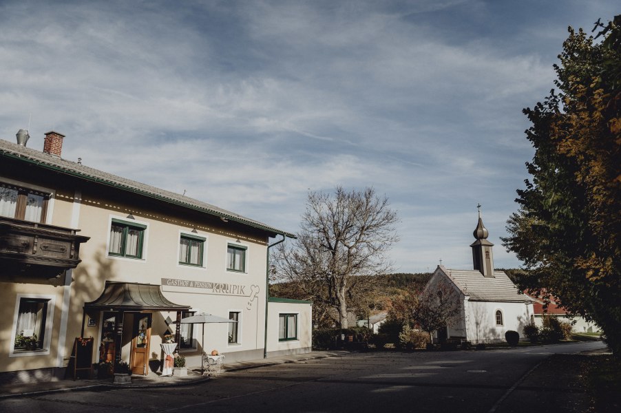 Gasthof und Kirche in Steinbach bei Nagelberg, umgeben von B&auml;umen und blauem Himmel.