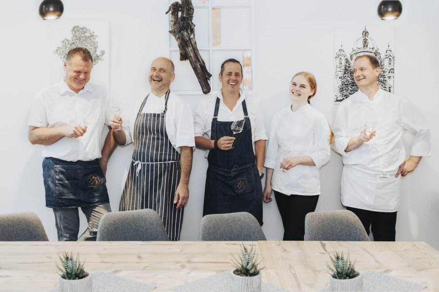 F&uuml;nf Personen in Kochkleidung lachen und halten Weingl&auml;ser in der Hand.